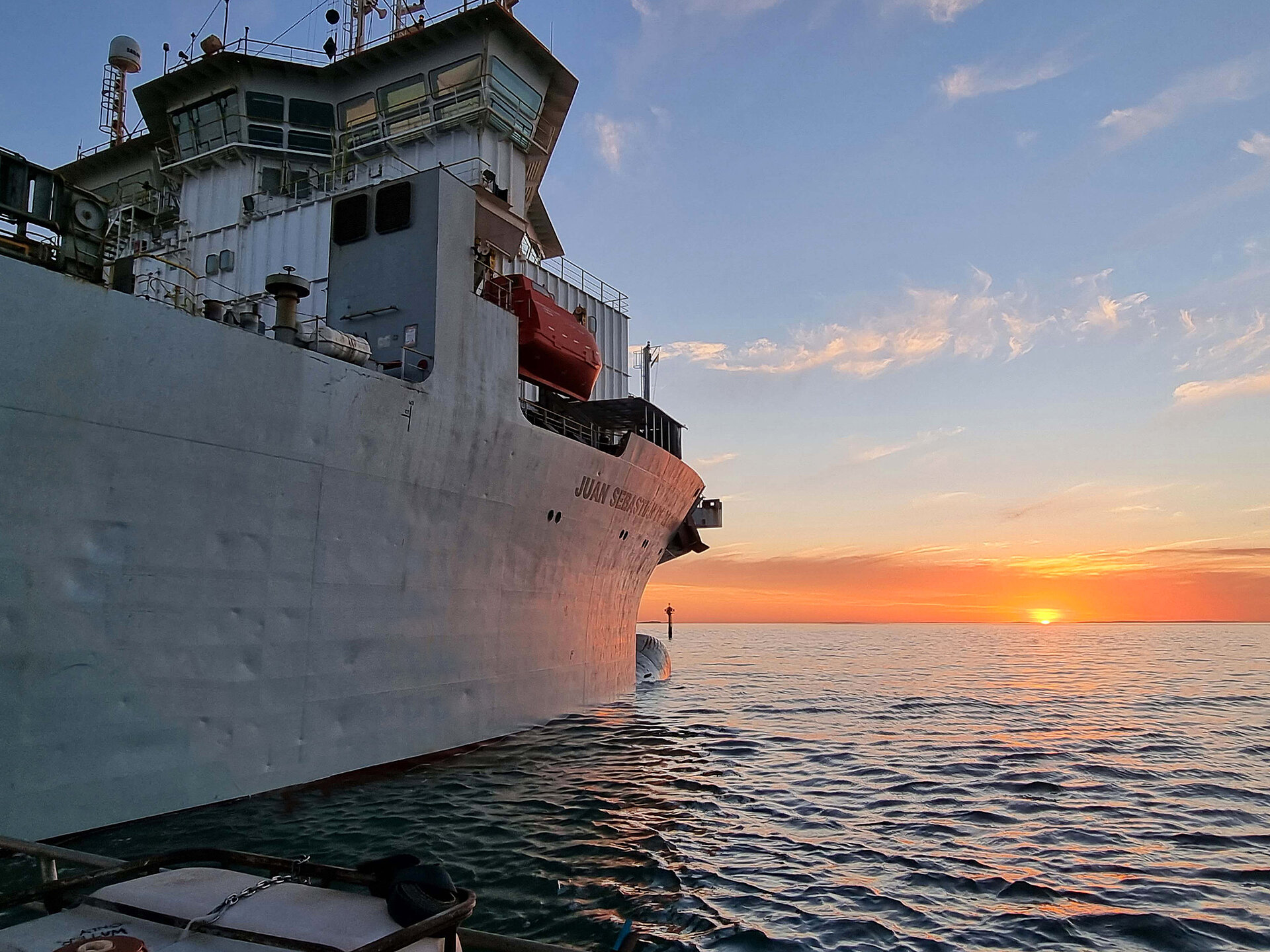 A ships hull seen from a small neighbouring boat with cabin visible at sunset